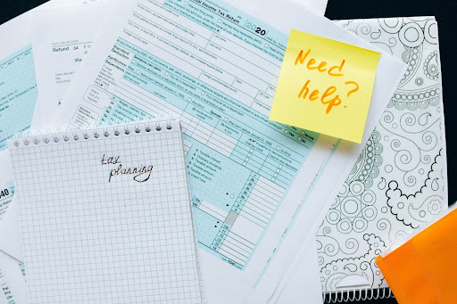 A note with the words “Need help?” and a notepad with “tax planning” sitting on top of a tax form.